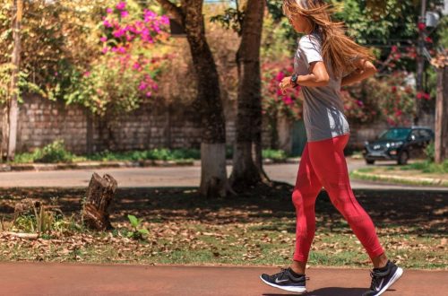 A woman jogs on a path surrounded by trees and vibrant flowers, embodying a healthy lifestyle.