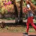 A woman jogs on a path surrounded by trees and vibrant flowers, embodying a healthy lifestyle.