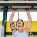 Focused woman doing a pull-up in a gym, featuring tattoos and workout equipment.